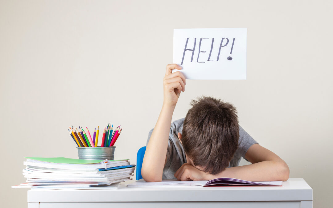 child with head on desk holding help sign